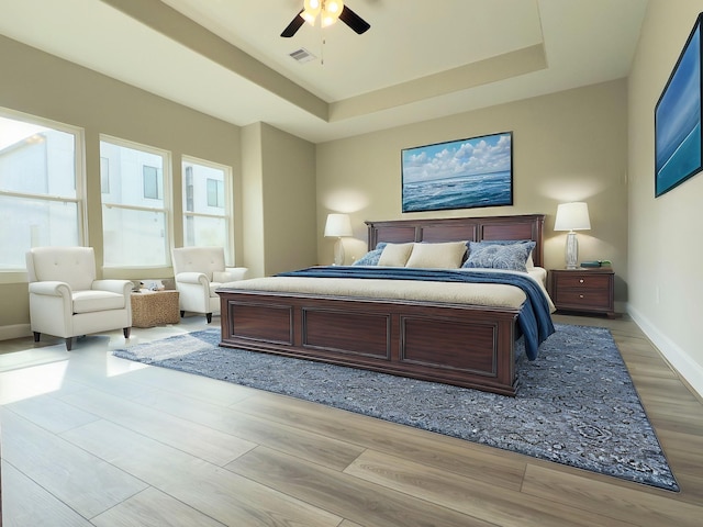 bedroom with a tray ceiling, baseboards, and light wood-type flooring