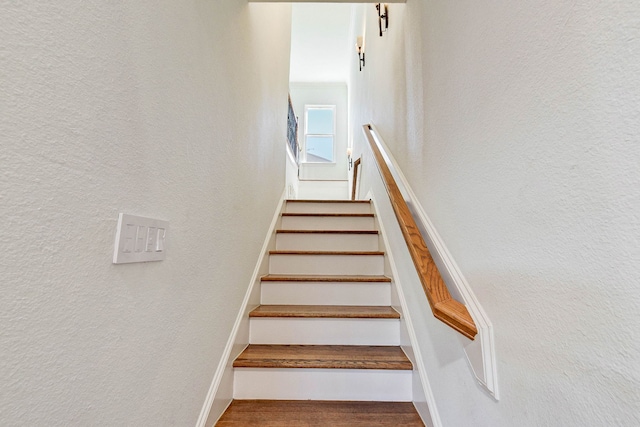 stairway featuring wood finished floors and a textured wall