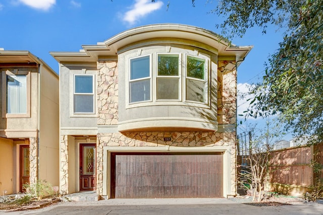 view of front of home featuring stone siding, driveway, fence, and a garage