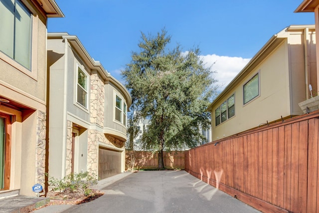 view of side of property with fence, a garage, stucco siding, and stone siding