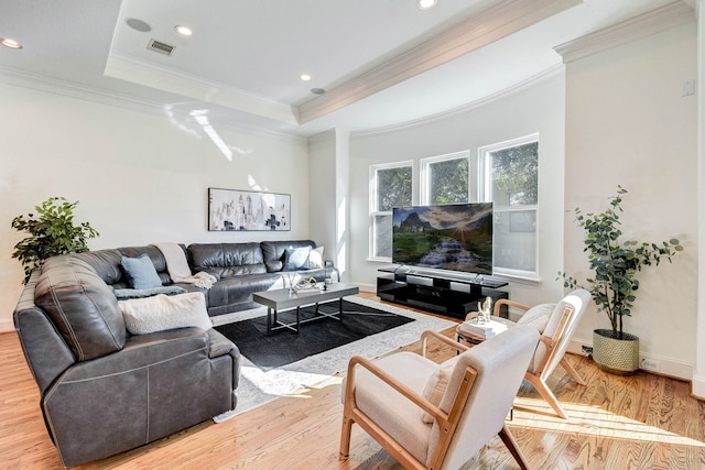 living area with a tray ceiling, visible vents, wood finished floors, and ornamental molding