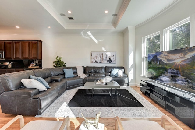 living room with visible vents, light wood-style flooring, a raised ceiling, and ornamental molding