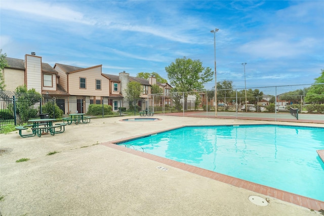 community pool featuring fence, a hot tub, a patio area, and a residential view