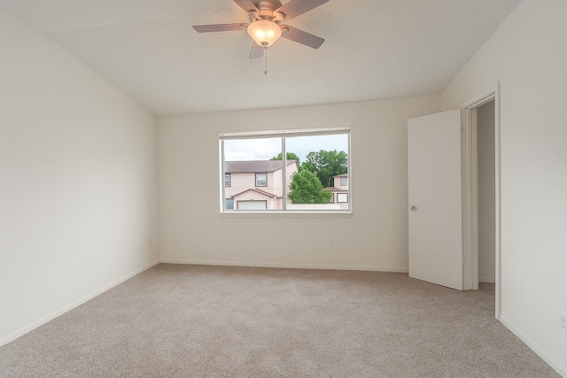 empty room featuring light colored carpet, a ceiling fan, and baseboards