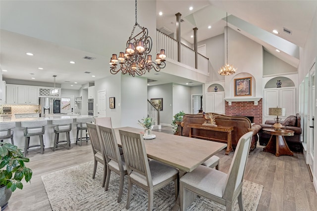 15050 Lake Paula Dr, Willis, TX 77318 - dining space with a chandelier, light wood-style flooring, high vaulted ceiling, recessed lighting, and a brick fireplace