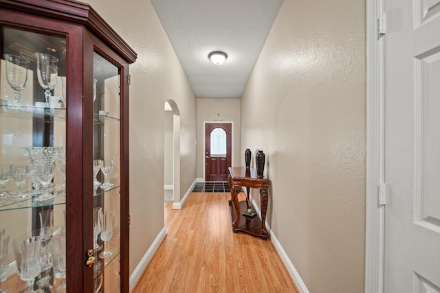doorway featuring light wood-style flooring, baseboards, arched walkways, and a textured wall