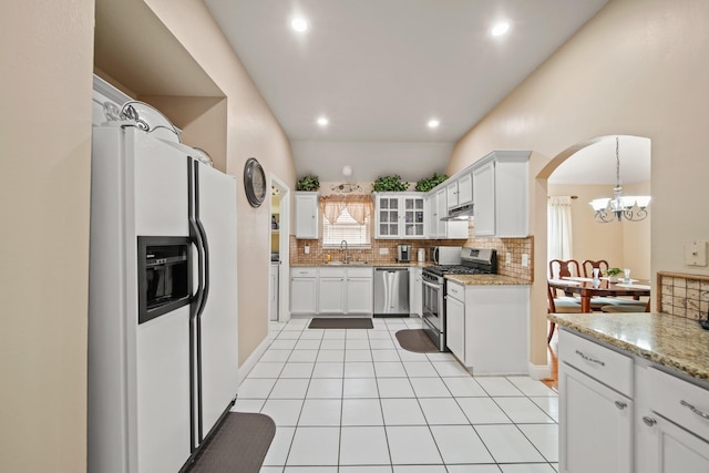 kitchen with an inviting chandelier, a sink, decorative backsplash, arched walkways, and stainless steel appliances