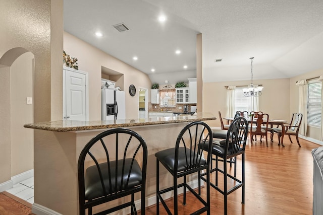 kitchen with light wood-type flooring, white fridge with ice dispenser, visible vents, a kitchen bar, and baseboards