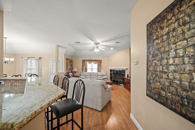 interior space featuring a tile fireplace, ceiling fan with notable chandelier, a textured ceiling, light wood-style floors, and vaulted ceiling