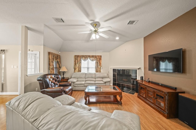living area with vaulted ceiling, light wood finished floors, a tiled fireplace, and visible vents