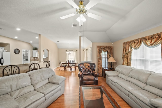 living room featuring light wood-style flooring, visible vents, ceiling fan with notable chandelier, vaulted ceiling, and arched walkways