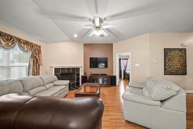 living area featuring ceiling fan, light wood-type flooring, and a tile fireplace