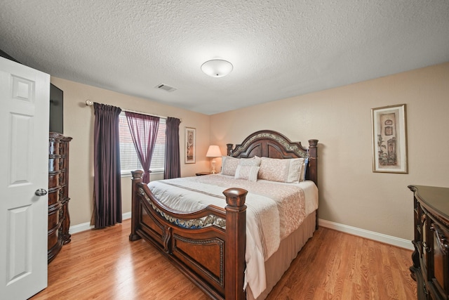 bedroom with light wood finished floors, a textured ceiling, visible vents, and baseboards