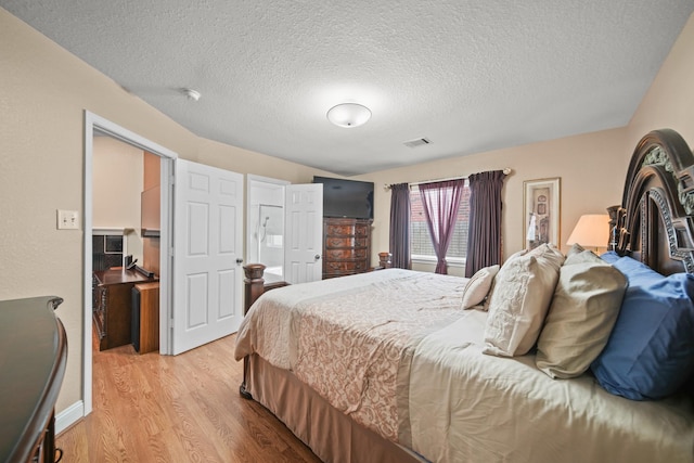bedroom featuring light wood-type flooring, visible vents, and a textured ceiling