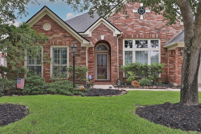 traditional home featuring roof with shingles, brick siding, and a front lawn