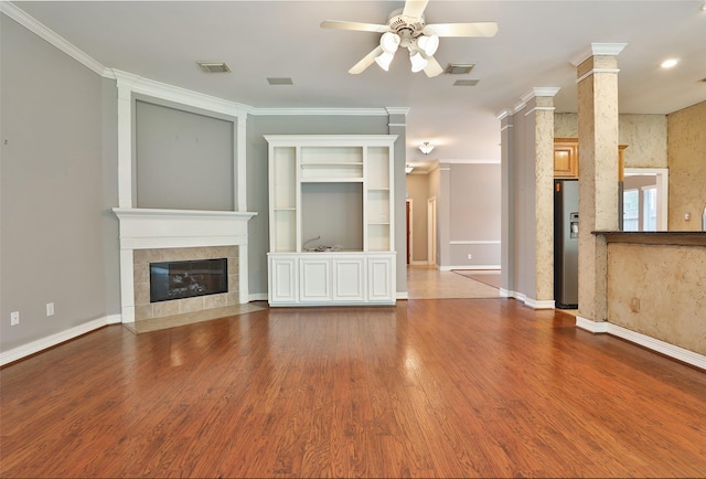 unfurnished living room featuring wood finished floors, visible vents, crown molding, a ceiling fan, and a tiled fireplace
