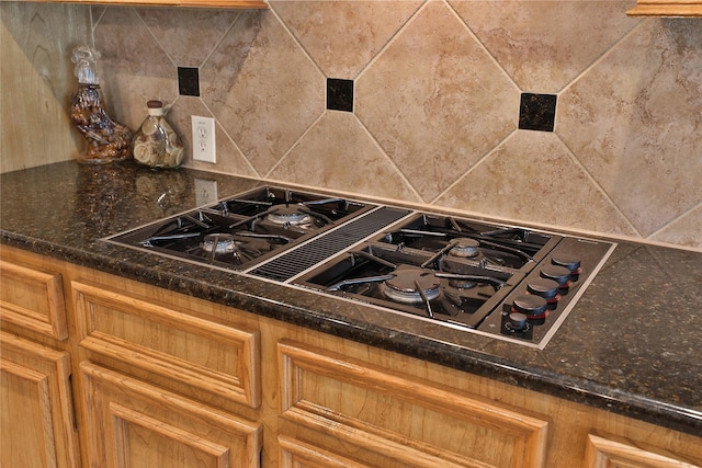 details featuring tasteful backsplash, dark stone countertops, and black gas stovetop