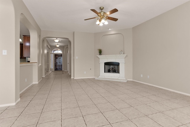 18239 Rustic Springs Dr, Tomball, TX 77375 - unfurnished living room with a ceiling fan, arched walkways, a fireplace with raised hearth, baseboards, and light tile patterned floors