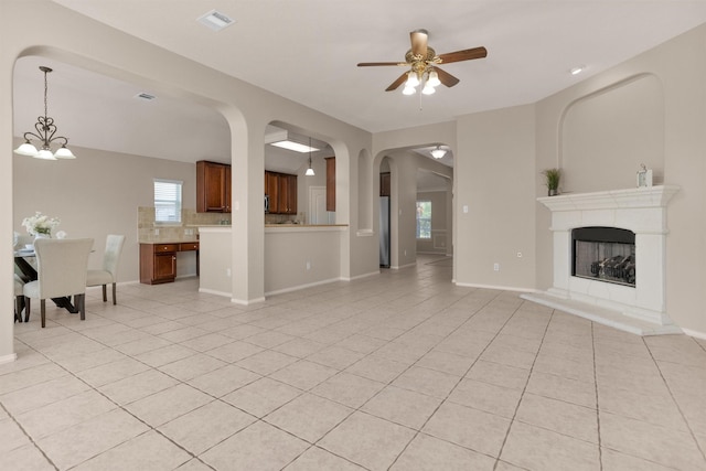 18239 Rustic Springs Dr, Tomball, TX 77375 - living area featuring light tile patterned floors, ceiling fan, a fireplace with raised hearth, baseboards, and arched walkways