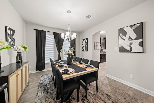 dining room featuring an inviting chandelier, light wood-style floors, visible vents, and arched walkways