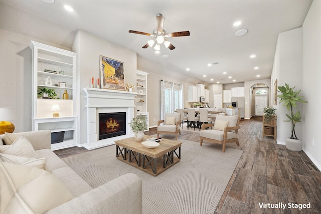 living area featuring wood finished floors, a lit fireplace, baseboards, ceiling fan, and recessed lighting