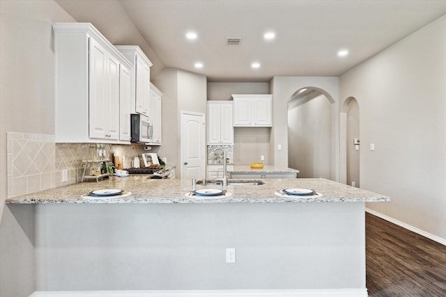 kitchen featuring a peninsula, a sink, stainless steel microwave, baseboards, and dark wood-style floors