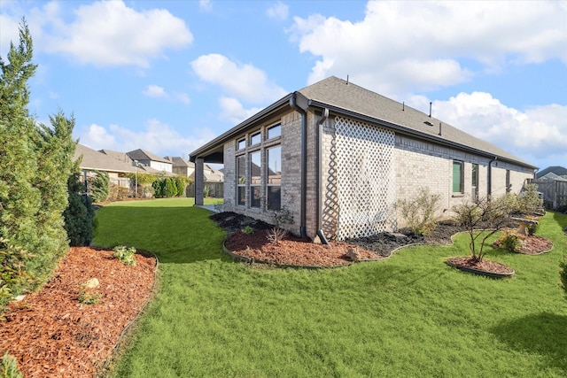 view of side of home featuring a lawn, brick siding, a shingled roof, and fence