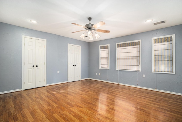 unfurnished bedroom featuring visible vents, wood finished floors, baseboards, and multiple closets