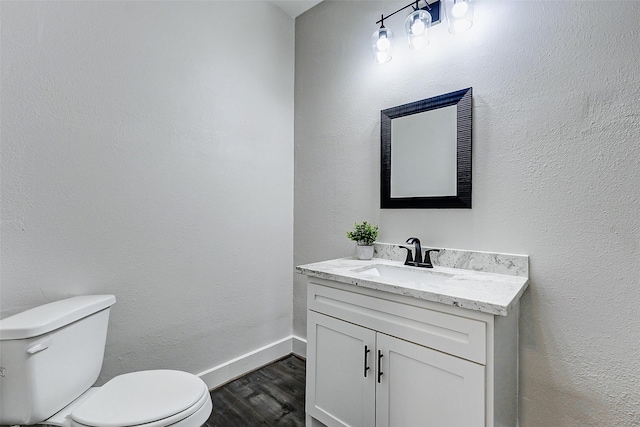 half bath with vanity, wood finished floors, toilet, and baseboards