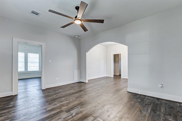 empty room with arched walkways, ceiling fan, dark wood-type flooring, and baseboards