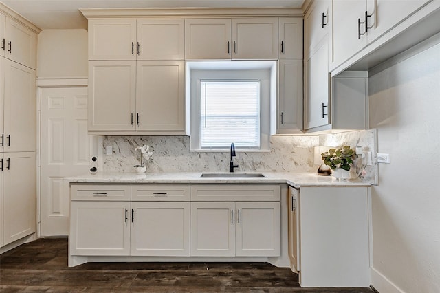 kitchen with decorative backsplash, light stone counters, dark wood-type flooring, and a sink