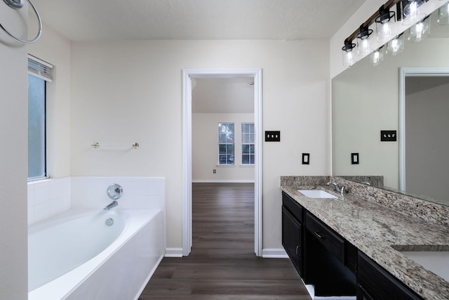 6902 Woodland Oaks, Magnolia, TX 77354 - bathroom with baseboards, a sink, a garden tub, double vanity, and wood finished floors