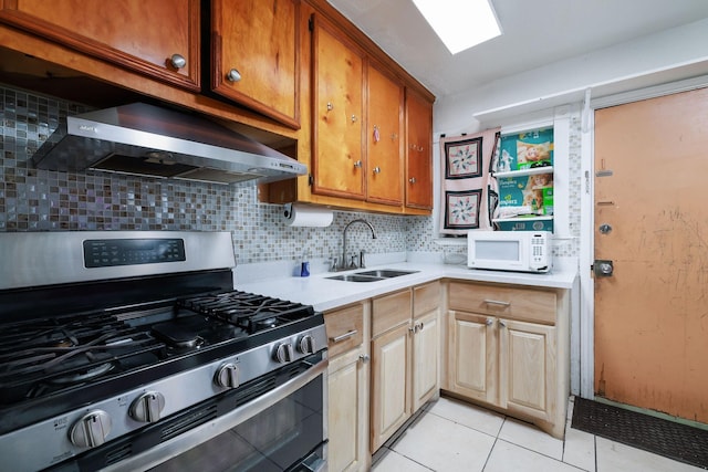 kitchen featuring a sink, wall chimney range hood, white microwave, gas stove, and light countertops