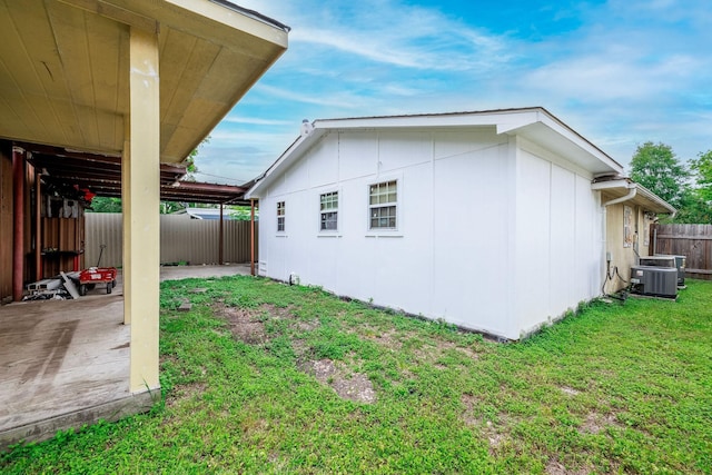view of side of property featuring a yard, a patio area, central air condition unit, a fenced backyard, and a carport