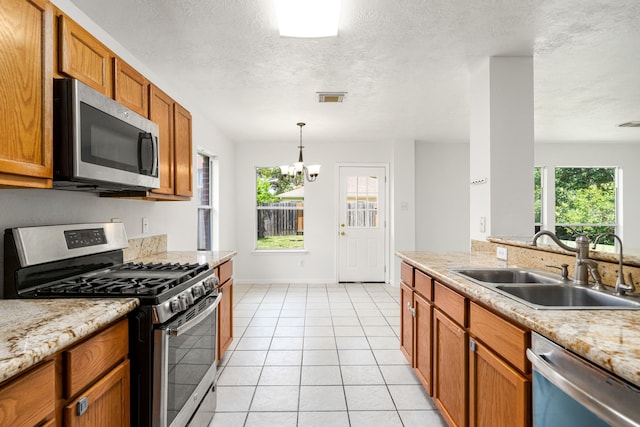 5315 Cilantro Ln, Baytown, TX 77521 - kitchen with stainless steel appliances, a sink, brown cabinets, a textured ceiling, and a chandelier