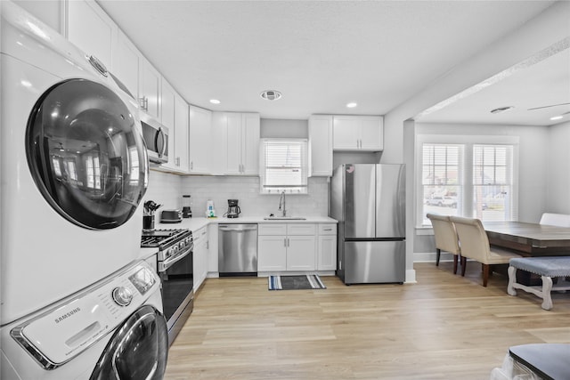 1802 Ursuline St, Galveston, TX 77550 - kitchen featuring stainless steel appliances, light wood finished floors, white cabinetry, stacked washing maching and dryer, and light countertops