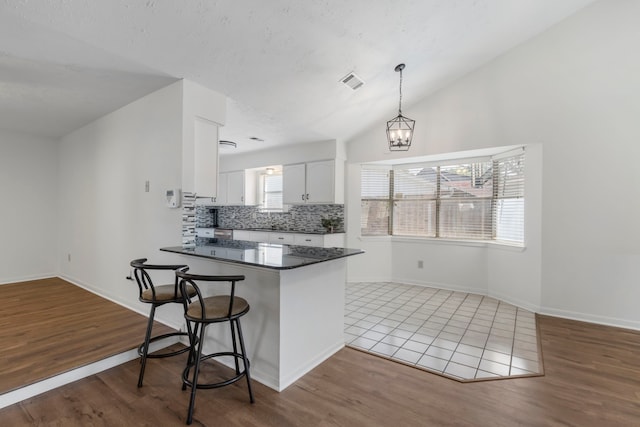 kitchen featuring dark countertops, a breakfast bar, white cabinetry, tasteful backsplash, and wood finished floors