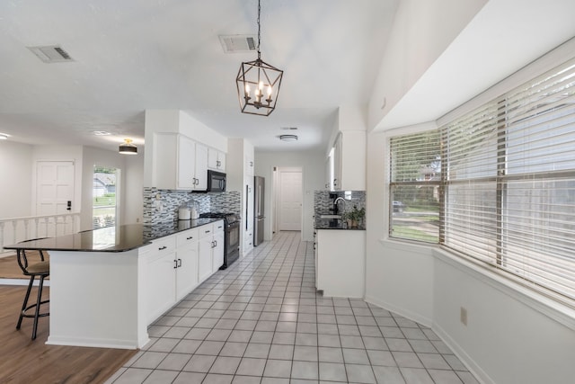 kitchen with black appliances, dark countertops, decorative backsplash, white cabinetry, and a kitchen breakfast bar