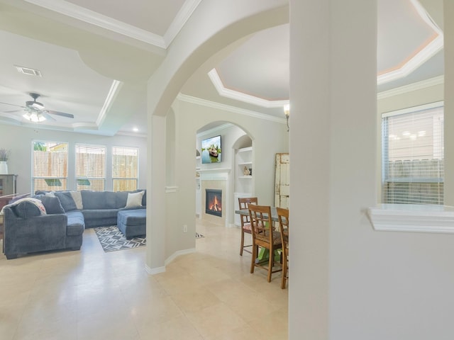 interior space featuring a tray ceiling, ceiling fan, a fireplace, and arched walkways