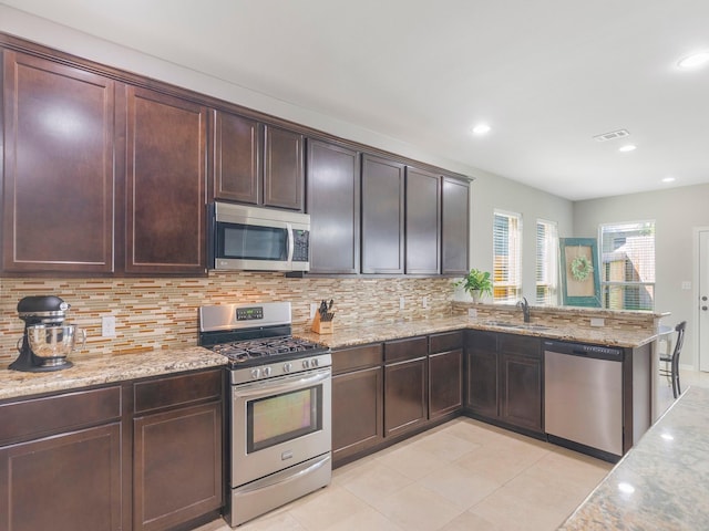 kitchen with a sink, stainless steel appliances, light stone counters, visible vents, and backsplash