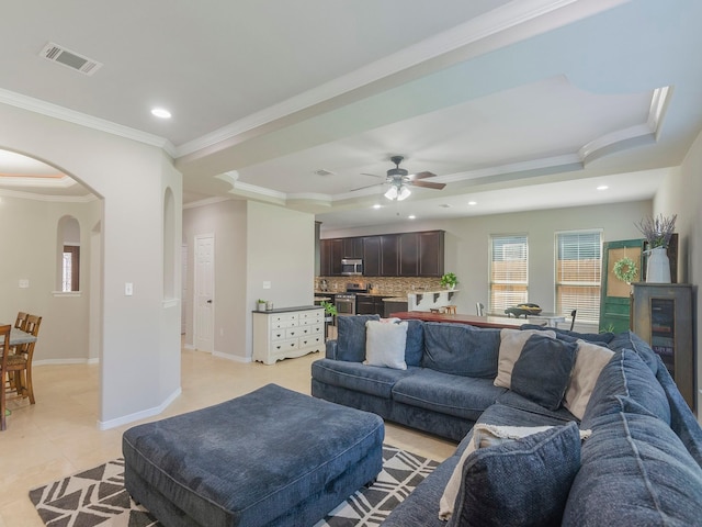 living area featuring crown molding, visible vents, a raised ceiling, and arched walkways