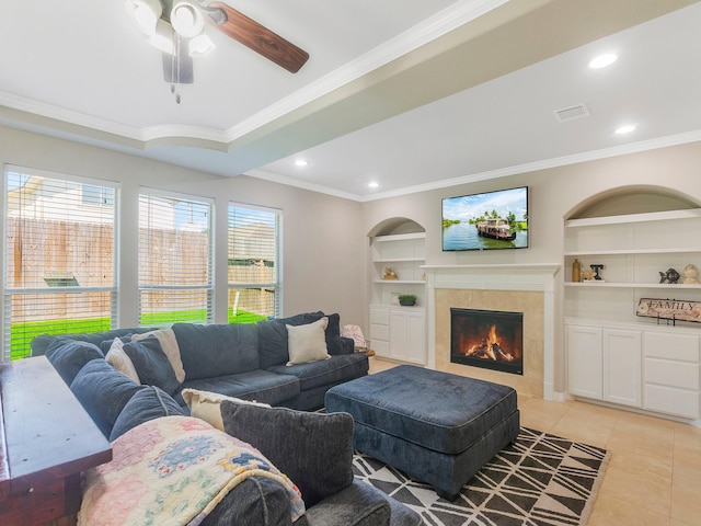 living room with ornamental molding, light tile patterned flooring, built in features, a ceiling fan, and a tile fireplace