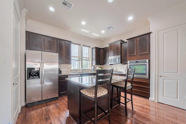 2303 Hadley St, Houston, TX 77003 - kitchen featuring appliances with stainless steel finishes, dark brown cabinets, a breakfast bar area, a sink, and backsplash