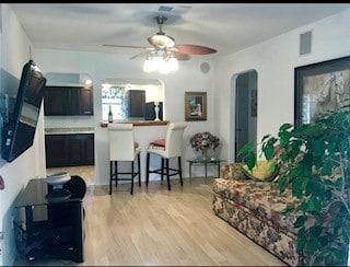 living room with light wood-type flooring, visible vents, ceiling fan, and arched walkways
