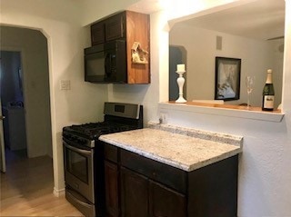 kitchen with dark brown cabinetry, black microwave, stainless steel range with gas cooktop, light wood-style floors, and light countertops
