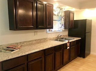 kitchen with freestanding refrigerator, light wood-style floors, dark brown cabinets, and a sink