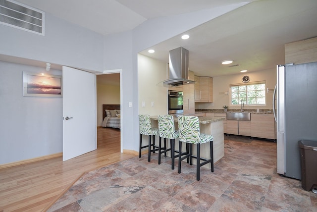 kitchen with freestanding refrigerator, visible vents, a sink, a peninsula, and wall chimney exhaust hood
