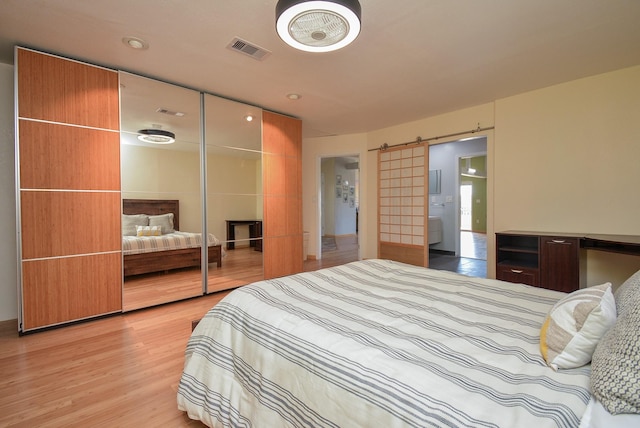 bedroom with light wood-style floors, visible vents, and a barn door