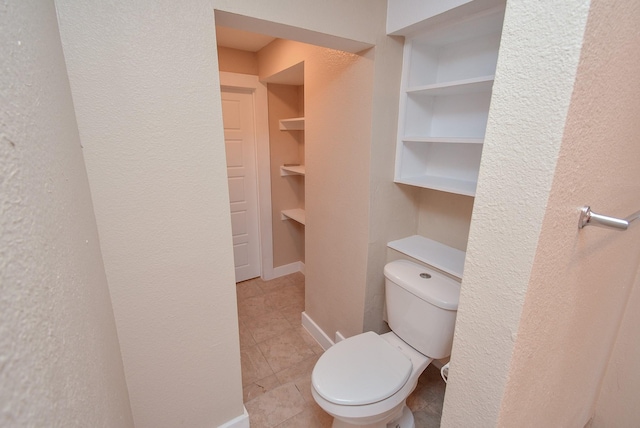 bathroom featuring toilet, built in shelves, tile patterned floors, and a textured wall