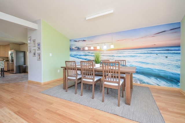 dining area featuring wood finished floors, vaulted ceiling, an accent wall, baseboards, and wallpapered walls